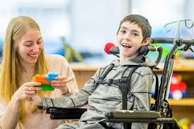 A therapist playing with building blocks alongside a boy in a support chair